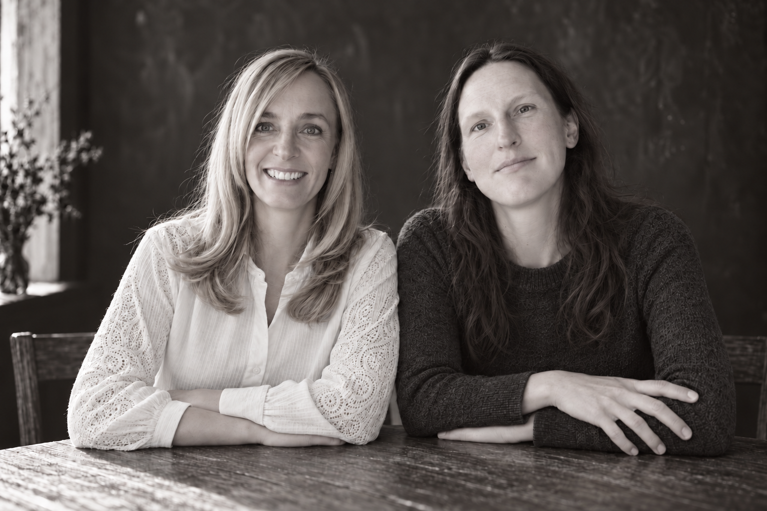 Jenny und Svenja sitzen gemeinsam an einem Tisch – Jenny im dunklen Strickpullover, Svenja in einer hellen Bluse